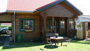 A wooden cabin with a red-tiled roof, a porch with a bench, and a small outdoor seating area with a table and chairs.