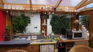 A cozy kitchen with a wooden countertop, a microwave, and a sink. There are wicker chairs and a potted plant.