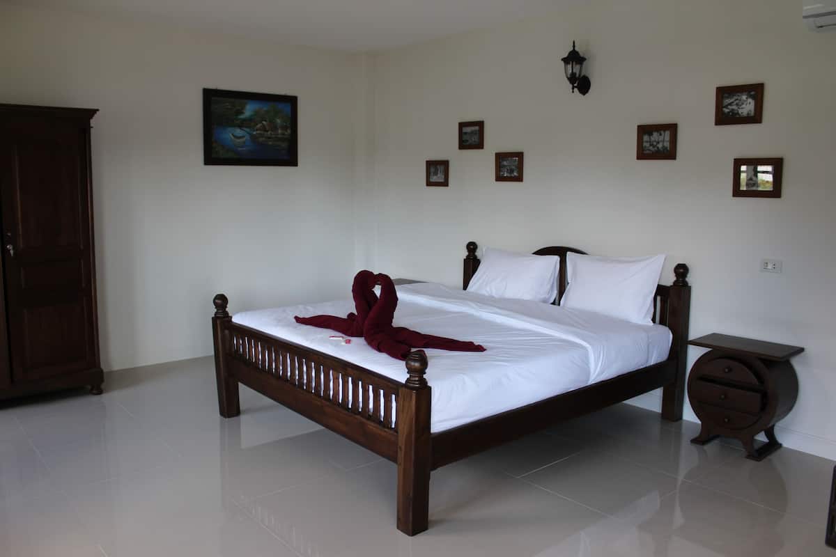 Uma cama bem arrumada com cabeceira de madeira, mesa de cabeceira com gaveta e luminária fixada na parede.