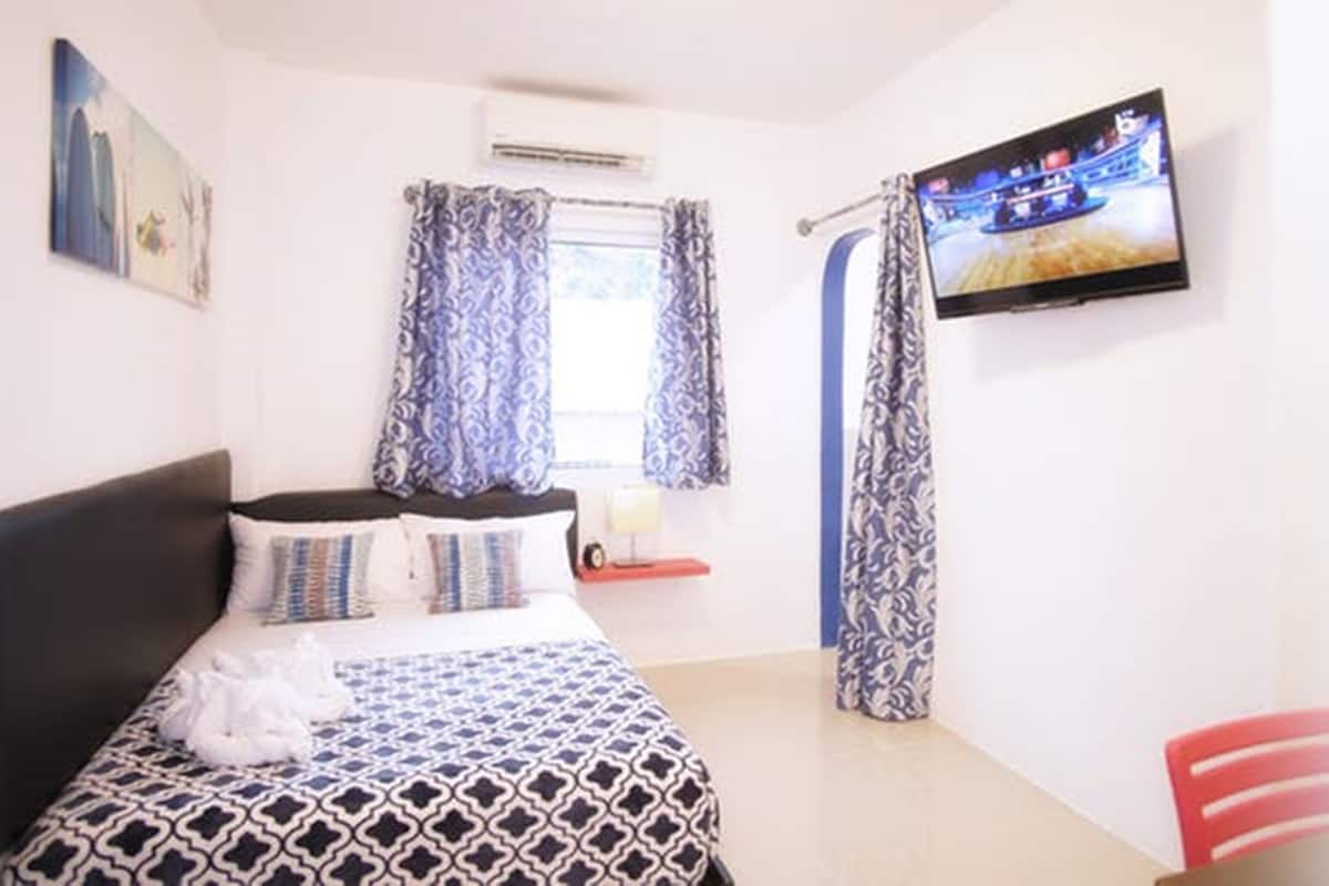 A bedroom with a bed, a television on the wall, and a window with curtains.