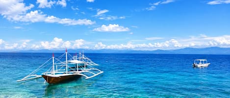 Une mer d’un bleu profond où voguent des bateaux, une côte rocheuse et des montagnes lointaines.