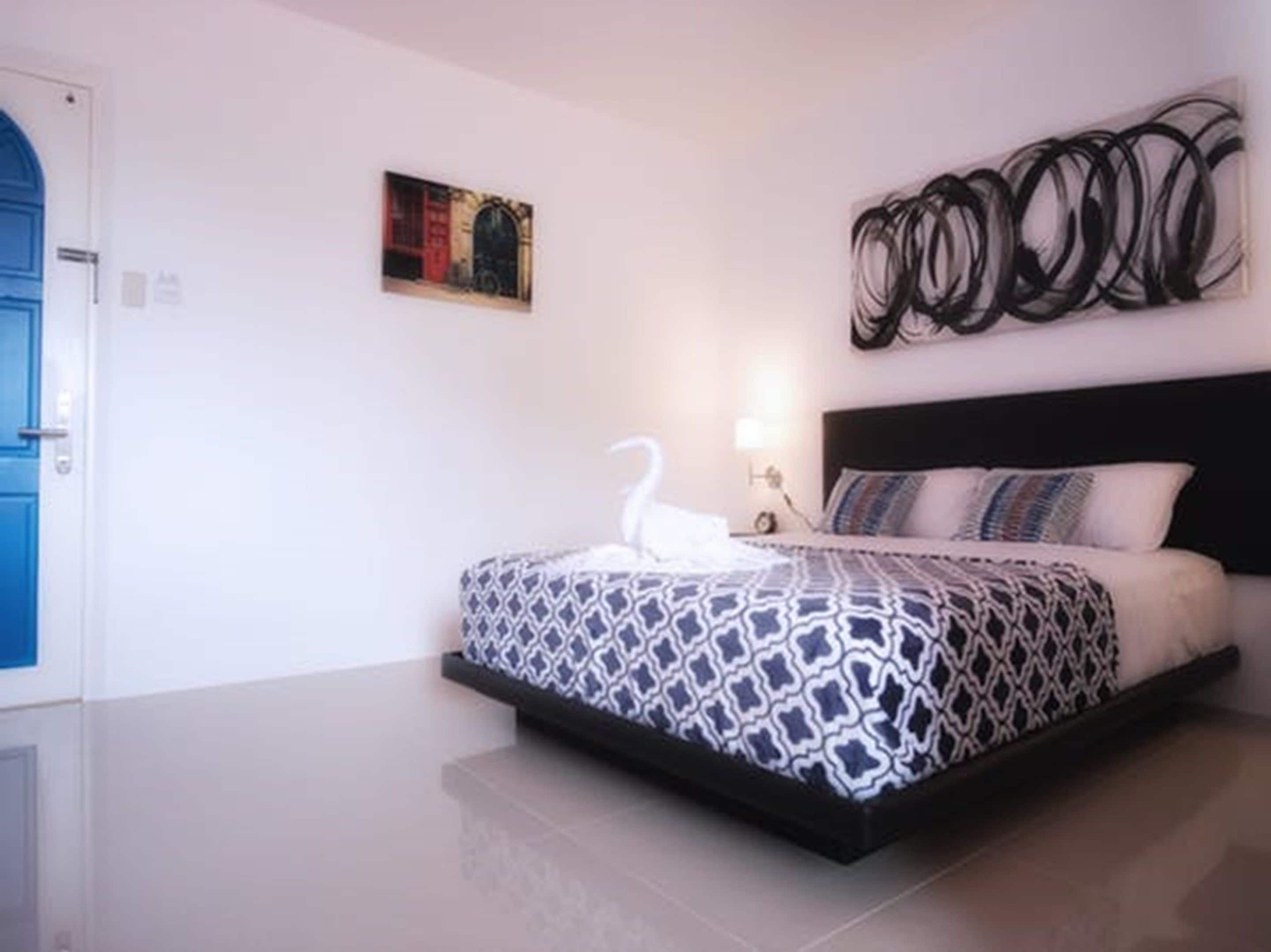 Een slaapkamer met een bed, een kunstwerk aan de muur en een blauwe deur.