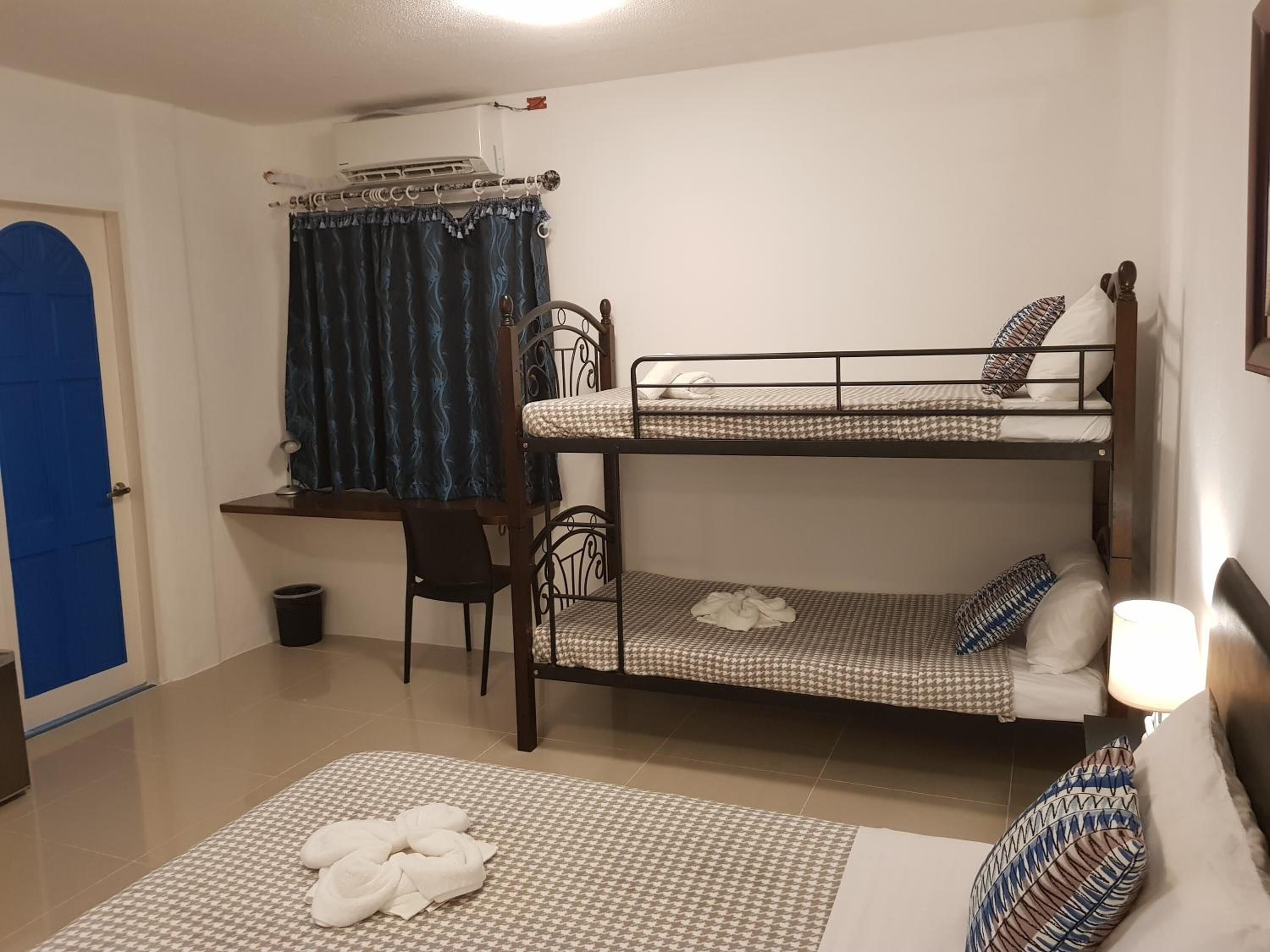 A dormitory room with bunk beds, a desk, a chair, a curtain, and a towel on the floor.