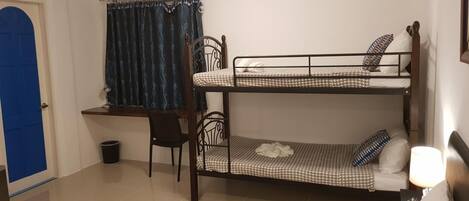A dormitory room with bunk beds, a desk, a chair, a curtain, and a towel on the floor.