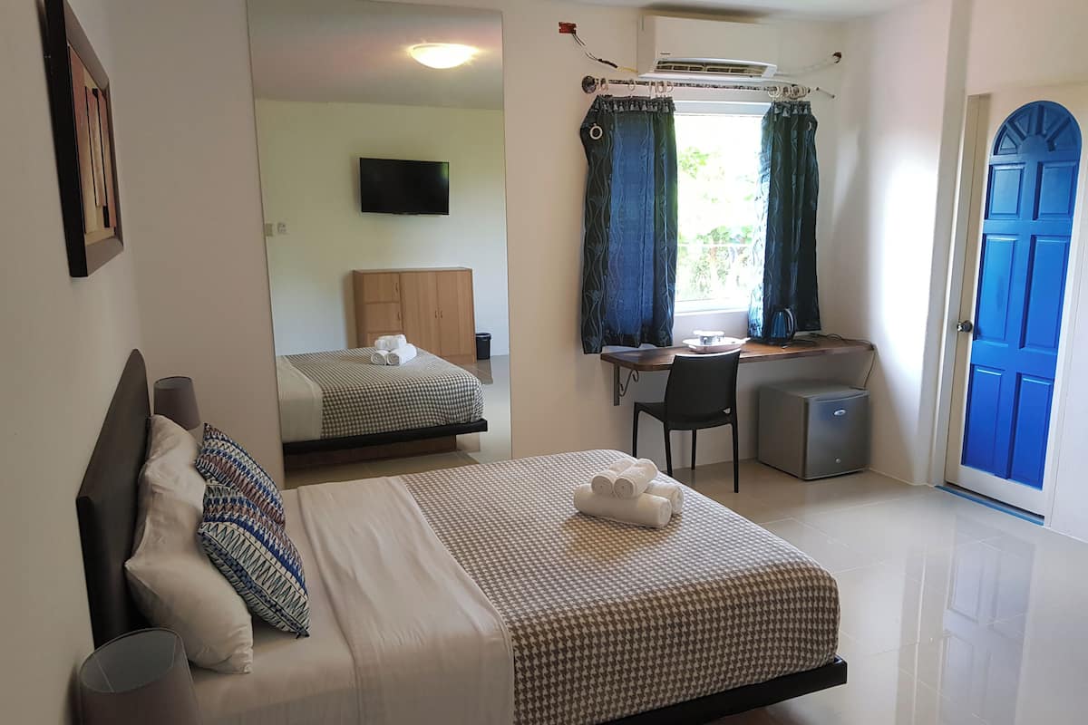 A hotel room with a bed, a desk, a chair, a TV, and a blue door.