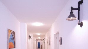 A long, well-lit hallway with white walls and a tiled floor, leading to a blue door at the end. - D' Gecko Hotel (Moalboal)