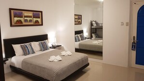 A hotel room with a large bed, a bedside table with a lamp, a mirror, and a bunk bed in the background. - D' Gecko Hotel (Moalboal)