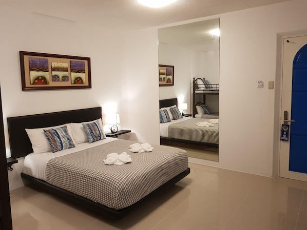 A hotel room with a large bed, a bedside table with a lamp, a mirror, and a bunk bed in the background. - D' Gecko Hotel (Moalboal)