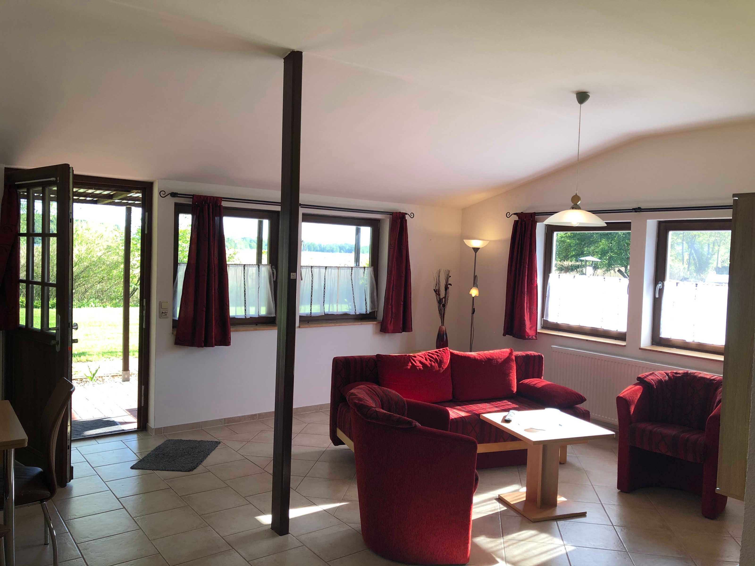 Ein Zimmer mit einem roten Sofa, einem Holztisch, einer Lampe und Blick durch große Fenster.