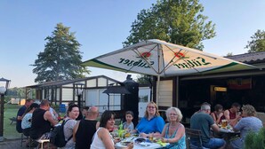 An outdoor dining area with tables and chairs, a large umbrella, and a building in the background. - FH 1A - Holiday home A (Dobbertin)
