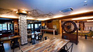 A restaurant interior with wooden tables, stone pillars, and a large decorative wheel. - Shin Kong Chao Feng Ranch And Resort (Fenglin)