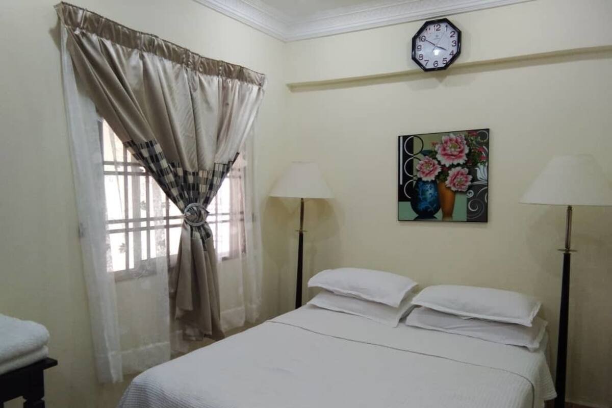 Un dormitorio con una cama, dos lámparas de noche, un reloj y un cuadro en la pared.