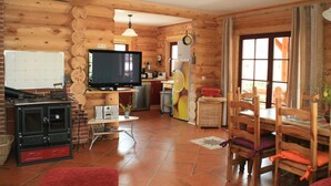 Interno di una baita in legno con televisione, mobili in legno, angolo cottura e un'ampia finestra.