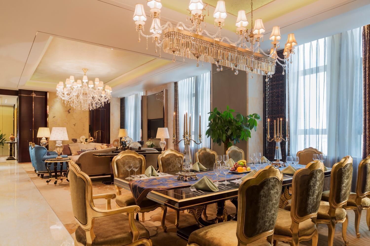A luxurious dining room with ornate chandeliers, a large dining table set for a meal, and elegant chairs.