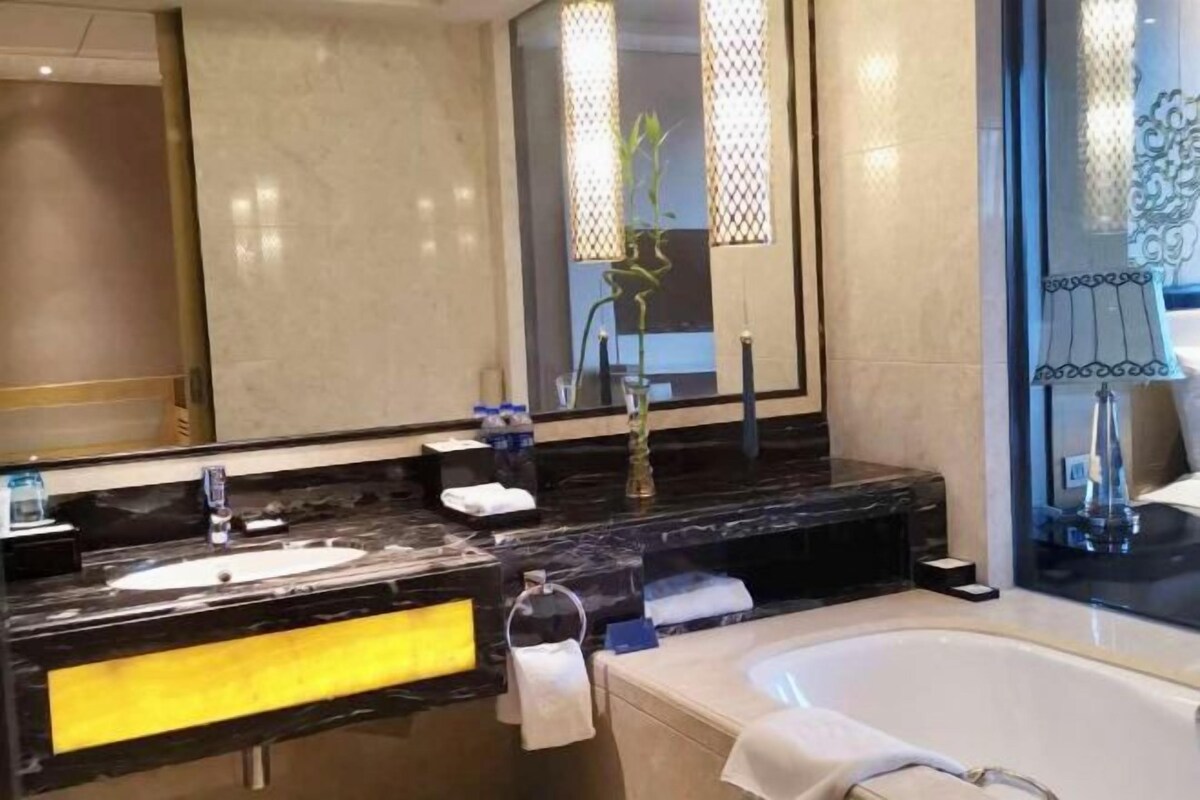 A modern bathroom with a large mirror, two sinks, a bathtub, and decorative lighting.
