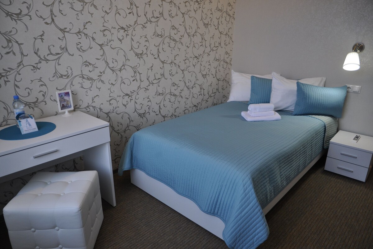 A neatly arranged hotel room with a bed, a bedside table, a desk, and a chair.