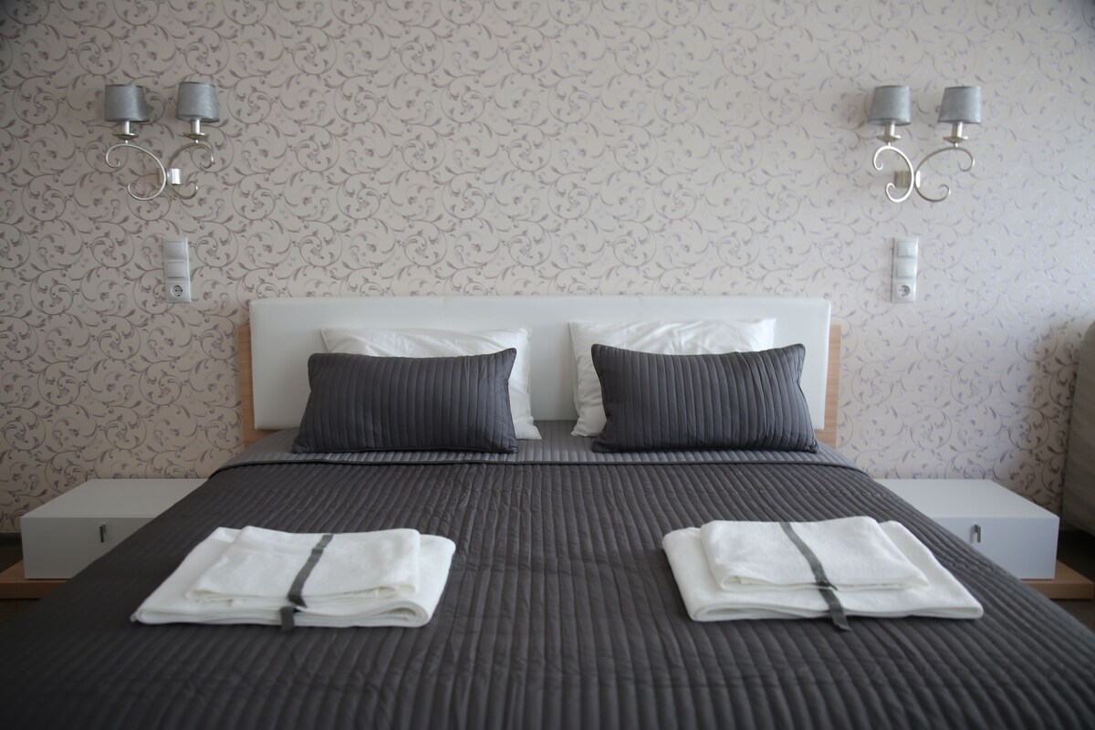 A neatly made bed with two pillows, a folded towel, and a bedside table with a lamp.