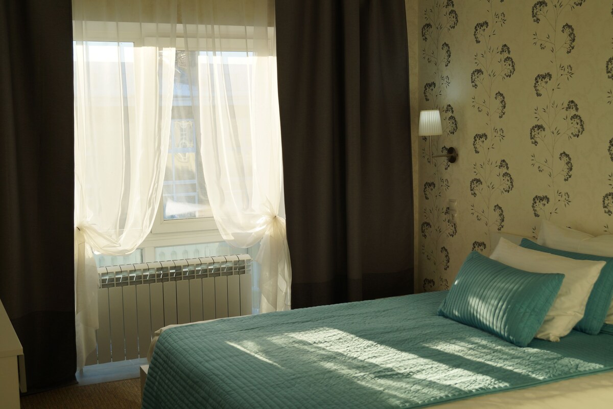 A bedroom with a bed, a radiator, and a window with sheer curtains.