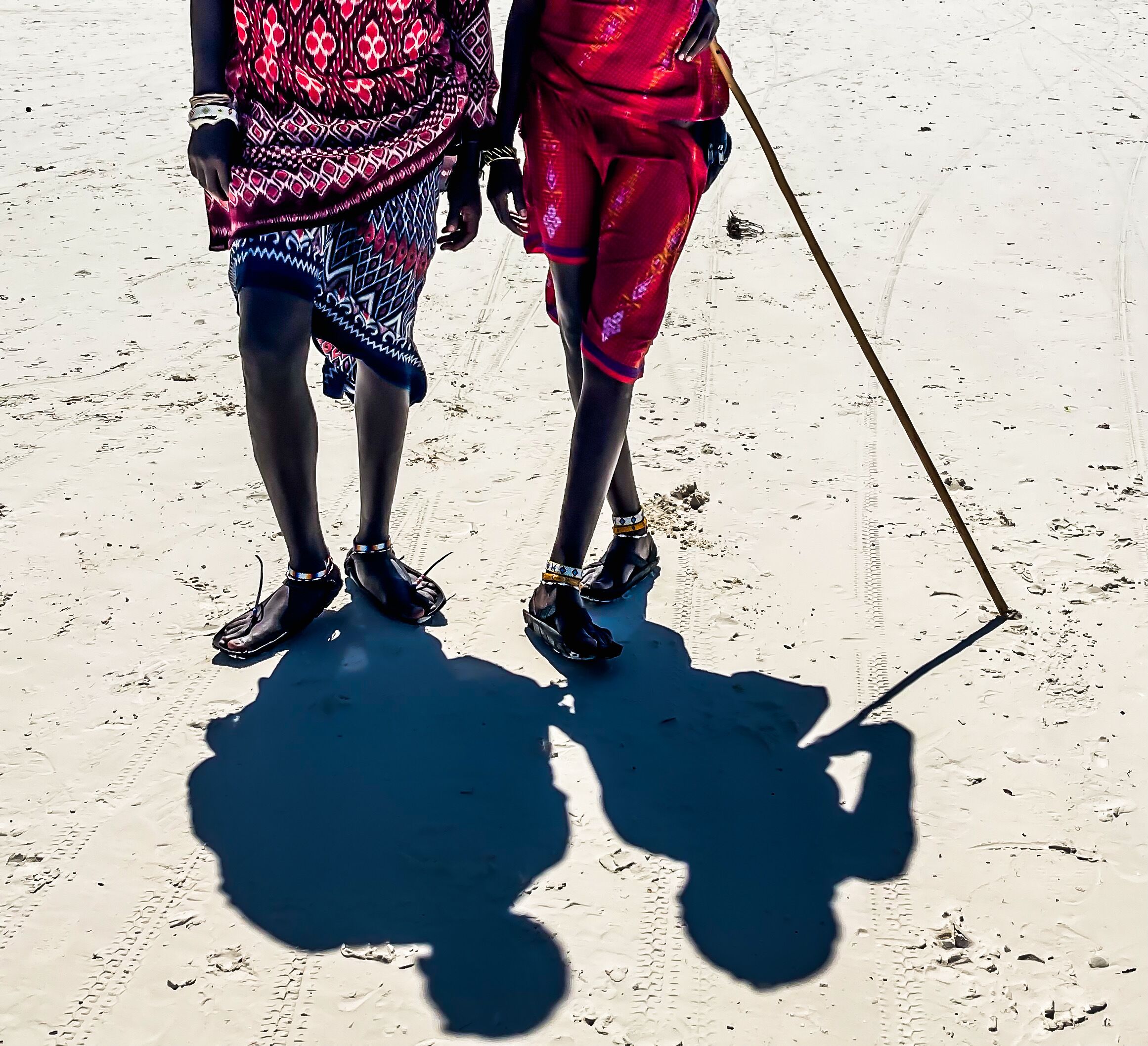 Two people standing on a sandy surface with shadows cast on the ground.
