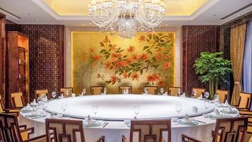 Un comedor formal con una mesa redonda dispuesta para una comida, rodeada de sillas, y una lámpara de araña grande colgando arriba.