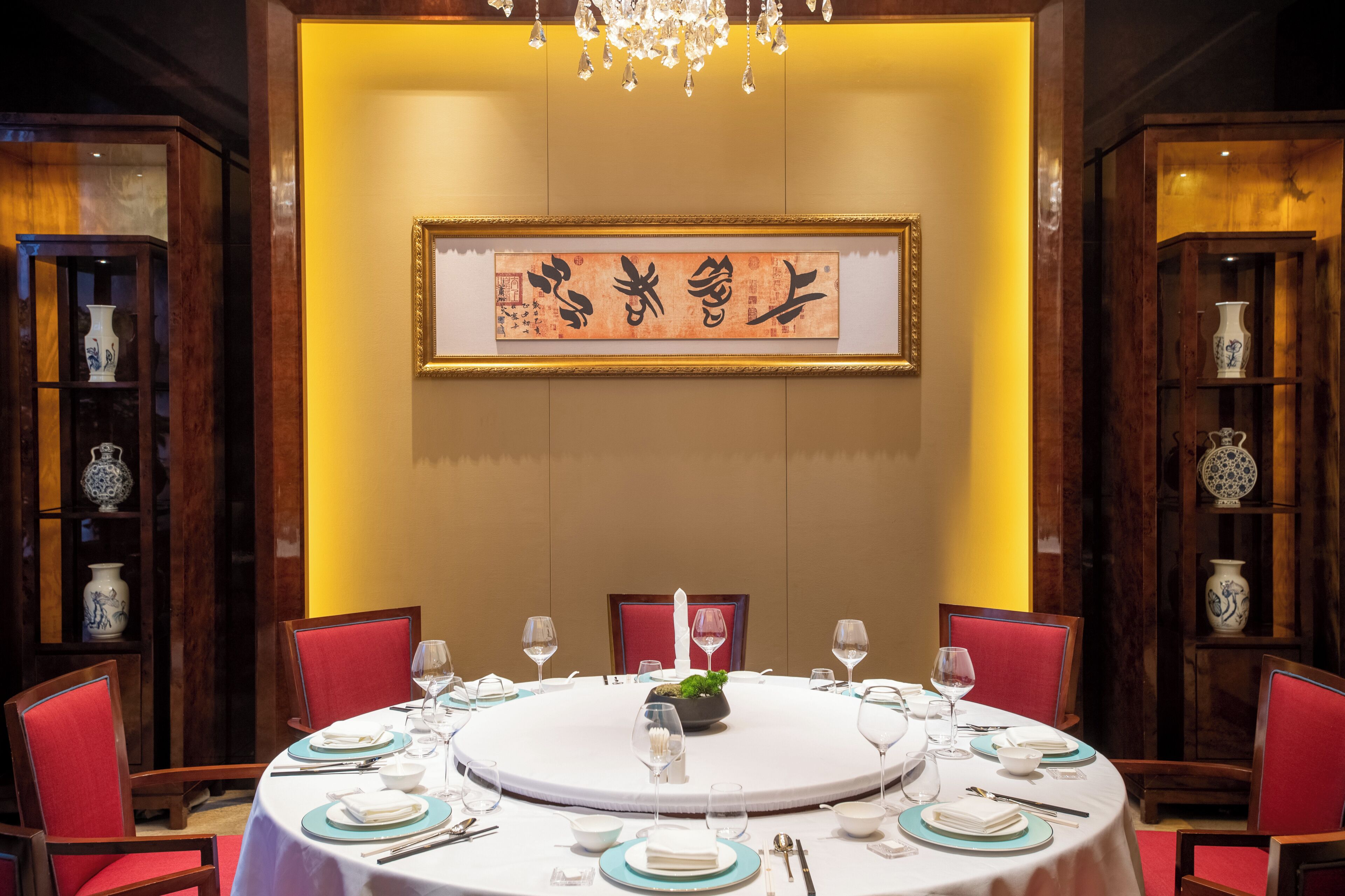 Mesa redonda para seis personas, con sillas rojas, una araña y arte de caligrafía china tradicional en la pared.