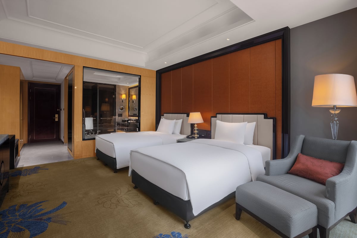 A hotel room with two beds, a sofa, a chair, a lamp, and a mirror.