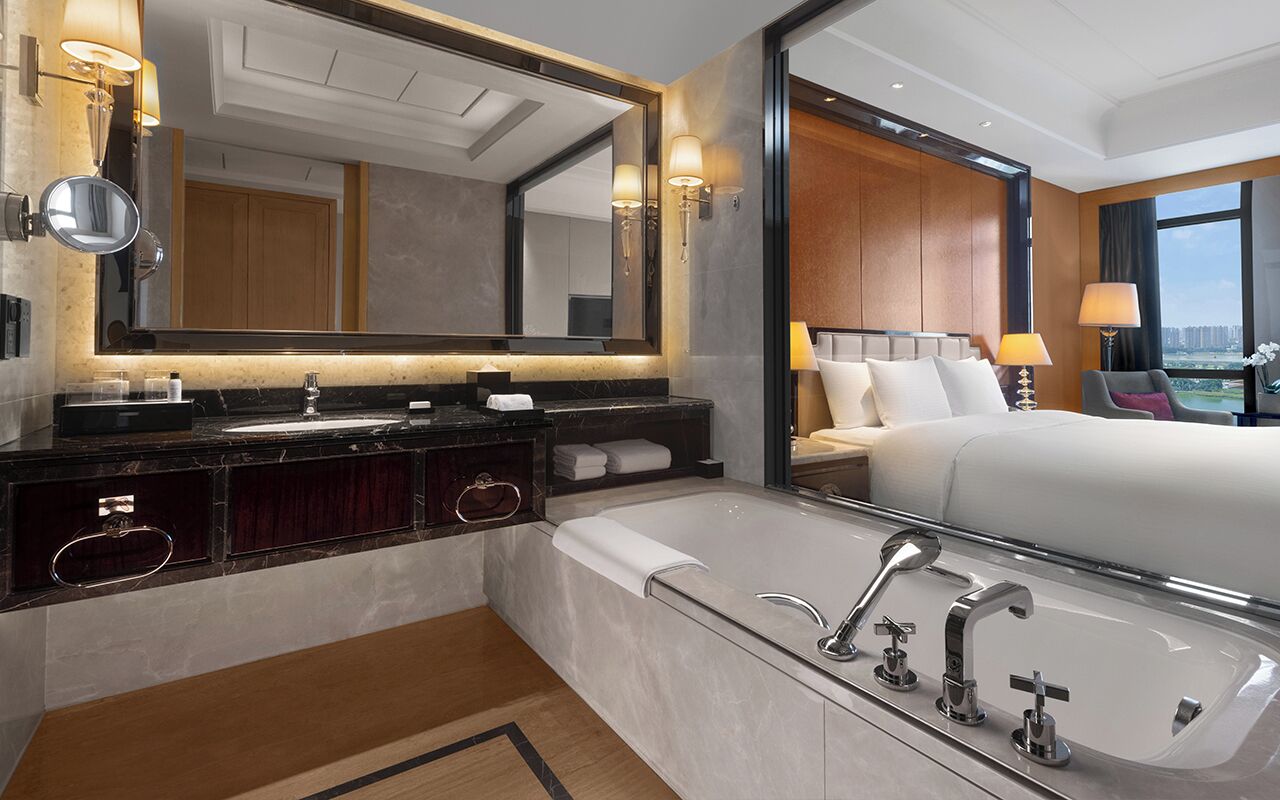 Een moderne hotelbadkamer met een grote spiegel, twee wasbakken, een badkuip en uitzicht op de stad door het raam.