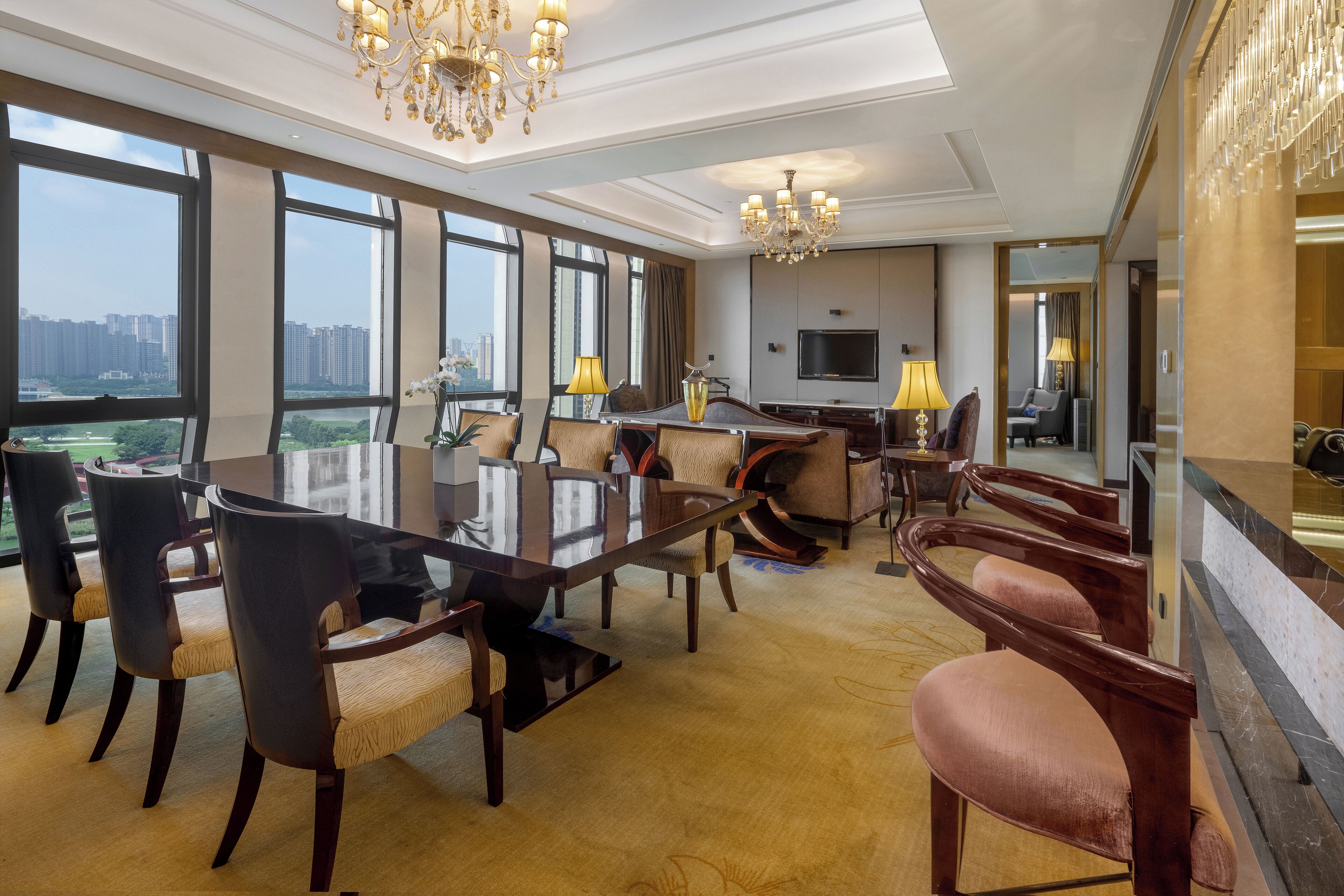 Une chambre d’hôtel spacieuse, dotée d’une grande table à manger, de sièges confortables, d’un téléviseur et offrant une vue sur la ville.