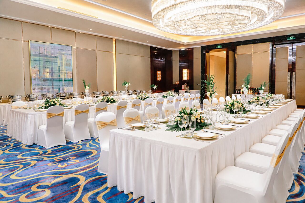 A banquet hall with round tables, white chairs, and a large chandelier.