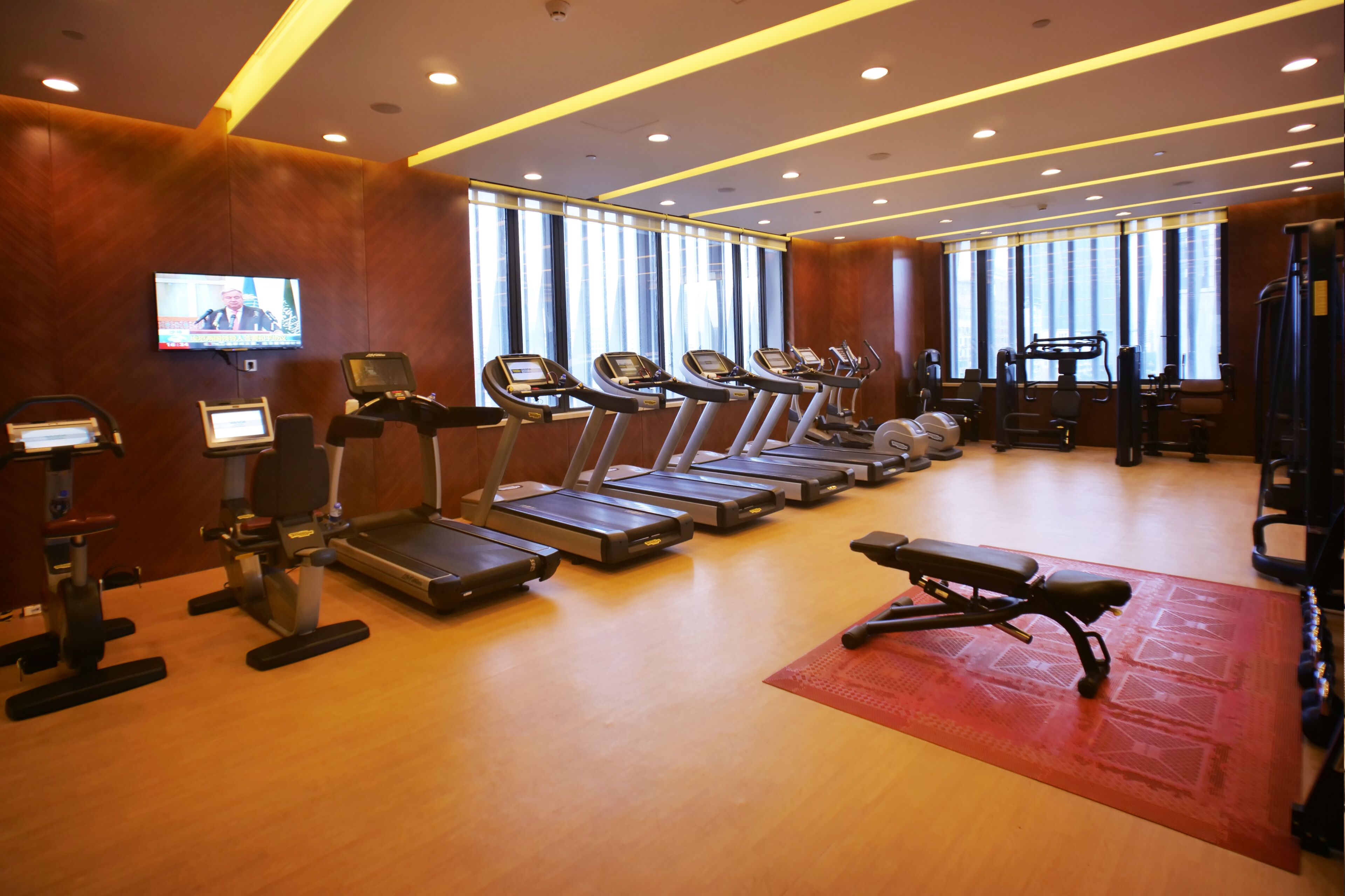 A gym with treadmills, exercise bikes, and a television screen.