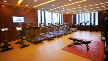 A gym with treadmills, exercise bikes, and a television screen.
