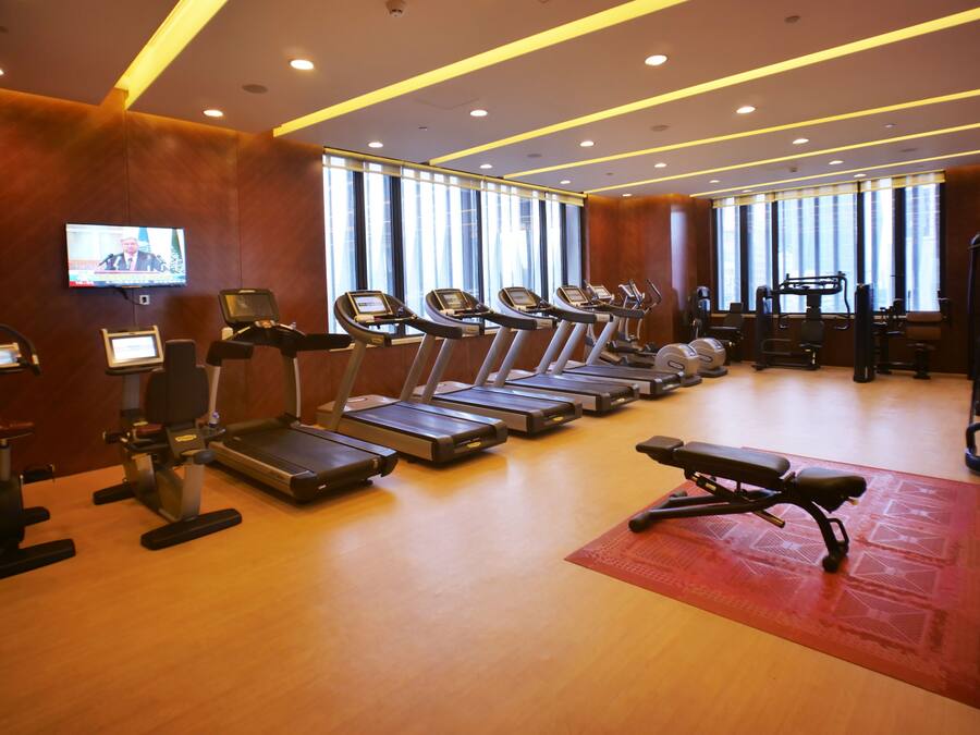 A gym with treadmills, exercise bikes, and a television screen.