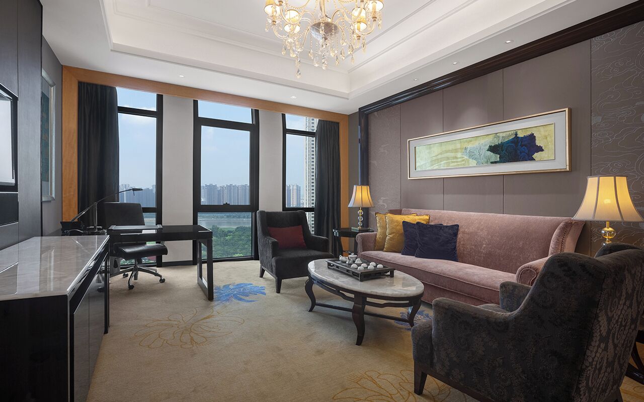A hotel room with a desk, office chair, sofa, armchair, and a coffee table.