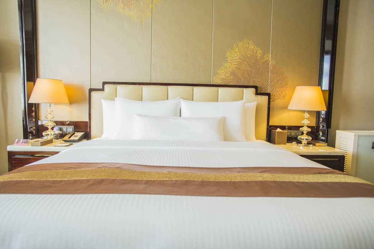 A large bed with a headboard, two bedside tables with lamps, and a nightstand with a telephone.