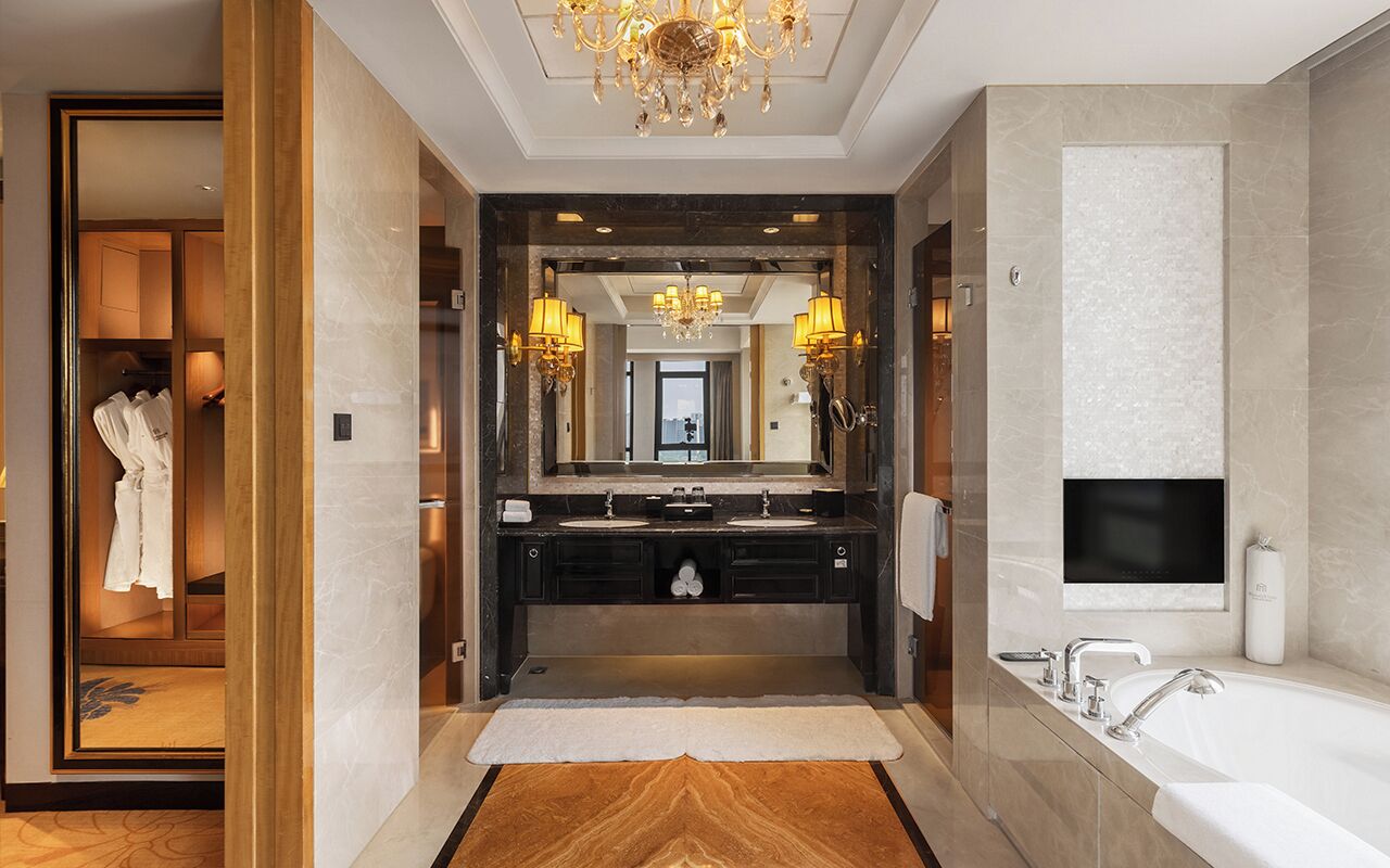 A luxurious bathroom with a double sink vanity, a large mirror, a chandelier, and a separate bathtub area.