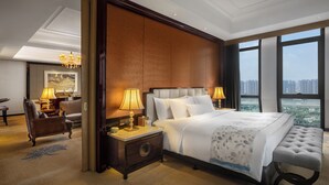 A spacious hotel room with a large bed, a sitting area with a chair and table, and a view of the city through large windows. - Wanda Vista Quanzhou (Quanzhou)