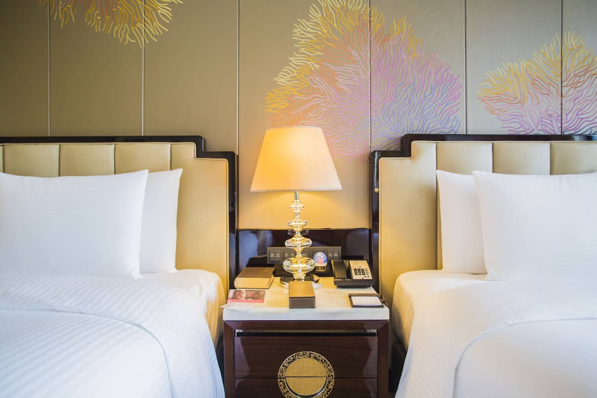 A hotel room with two beds, a nightstand with a lamp, a phone, and a decorative wall.