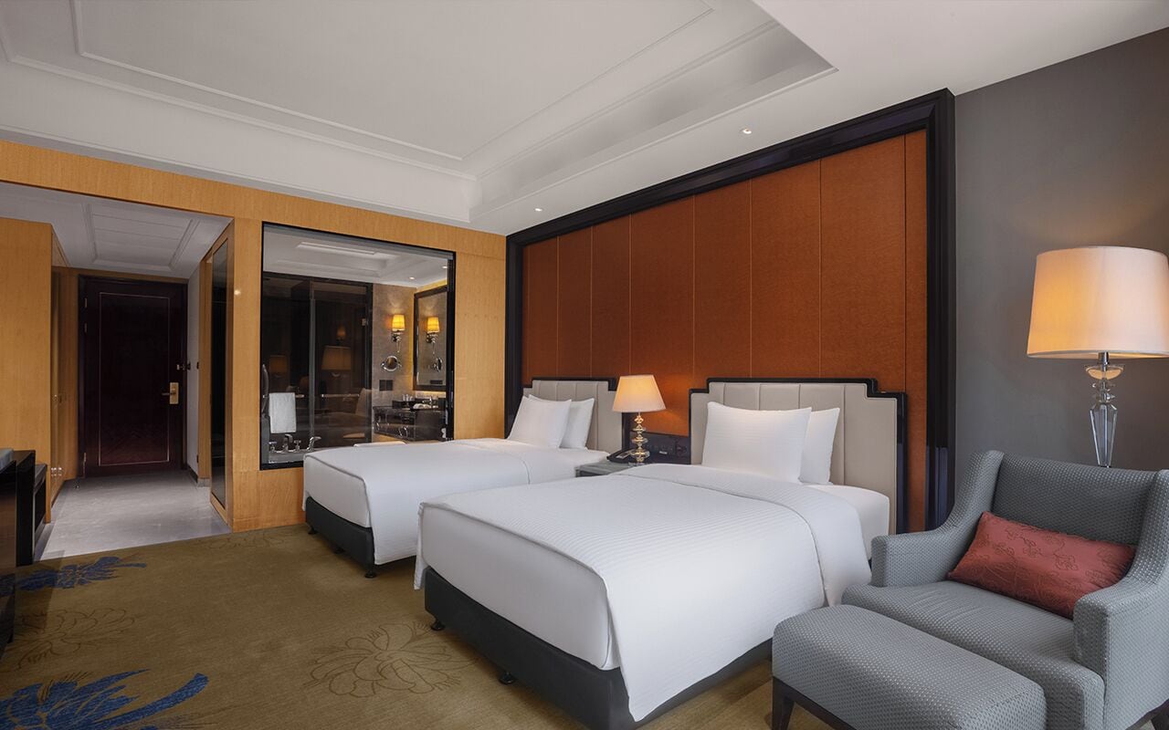 A hotel room with two beds, a sitting area, a mirror, and a lamp.