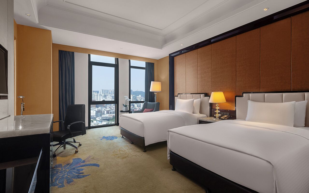 Une chambre d’hôtel avec deux lits, un bureau, une chaise, une lampe et une vue sur la ville.