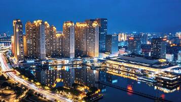 A cityscape at night with high-rise buildings and a river reflecting lights.