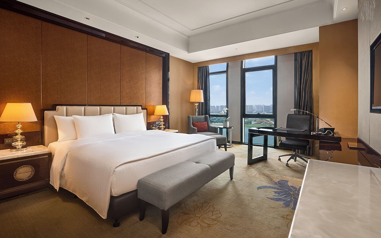A hotel room with a large bed, a desk, a chair, and a view of the city.