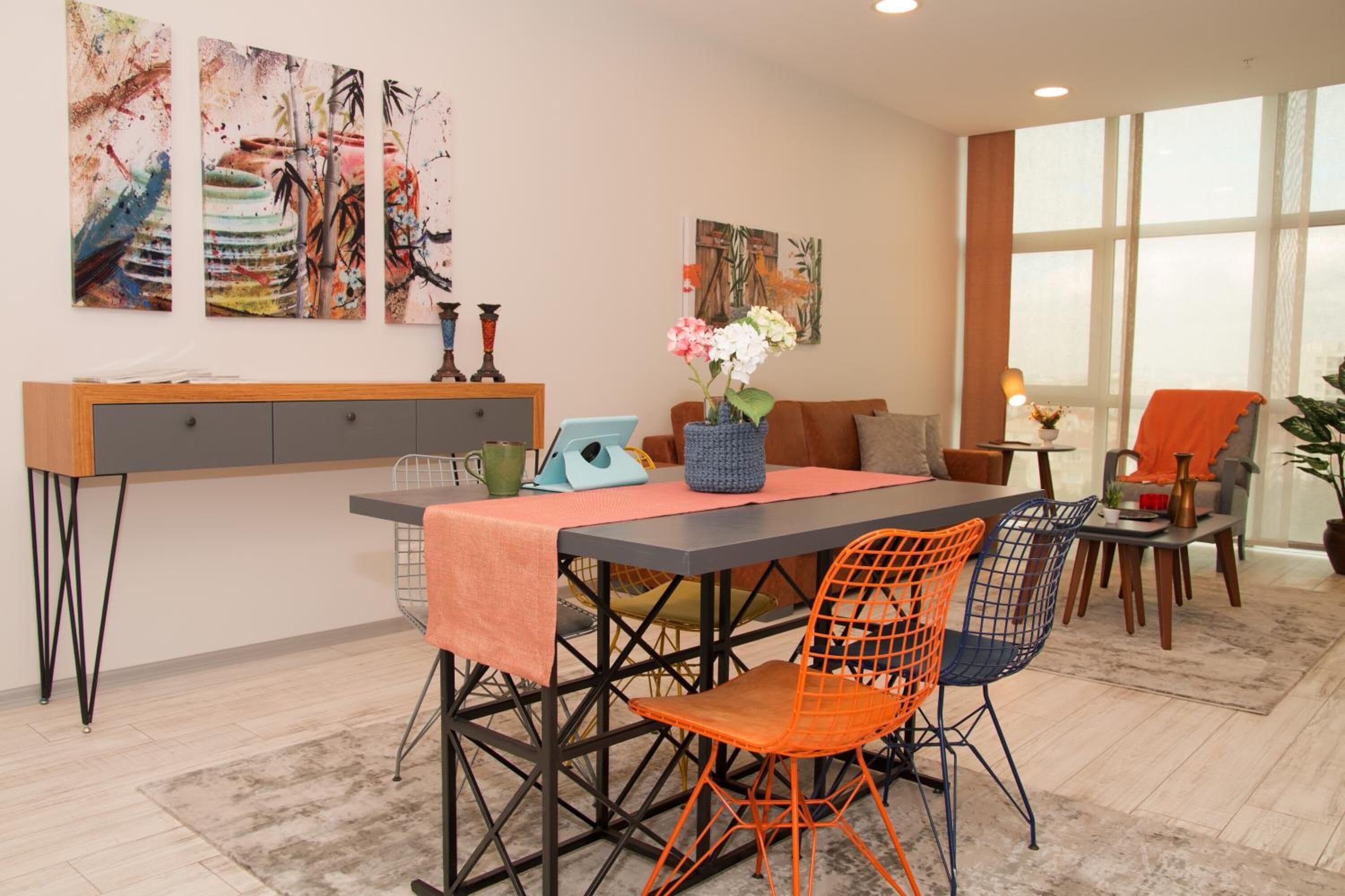 A modern living room with a dining table, orange and blue chairs, a sofa, and artwork on the walls.