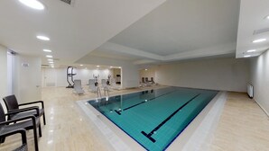 A large indoor swimming pool with a tiled floor, surrounded by exercise equipment and lounge chairs. - ZİN D Home Dudullu Suit Otel (Istanbul)