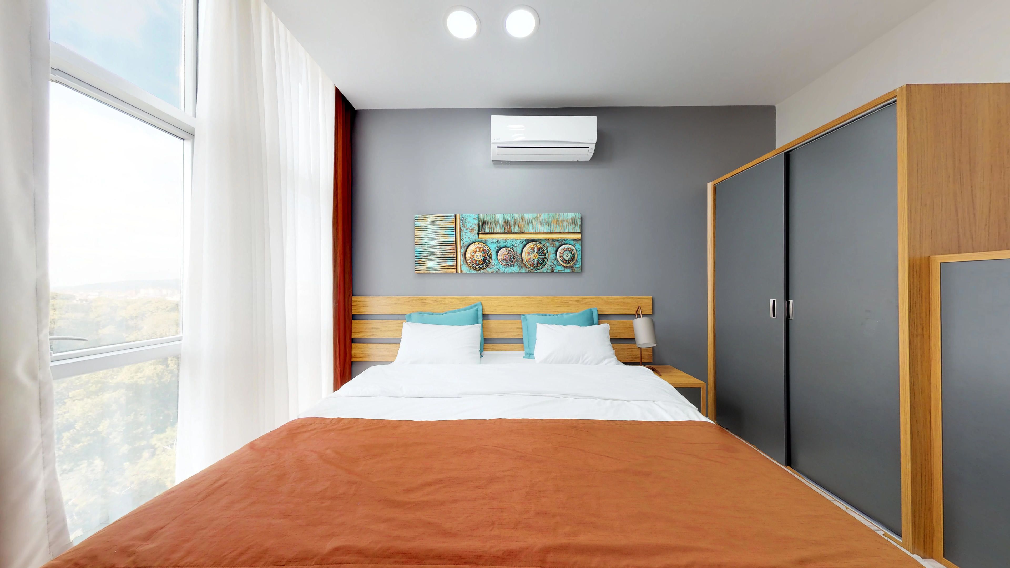 A bedroom with a bed, a wardrobe, a wall-mounted air conditioner, and a window with curtains.