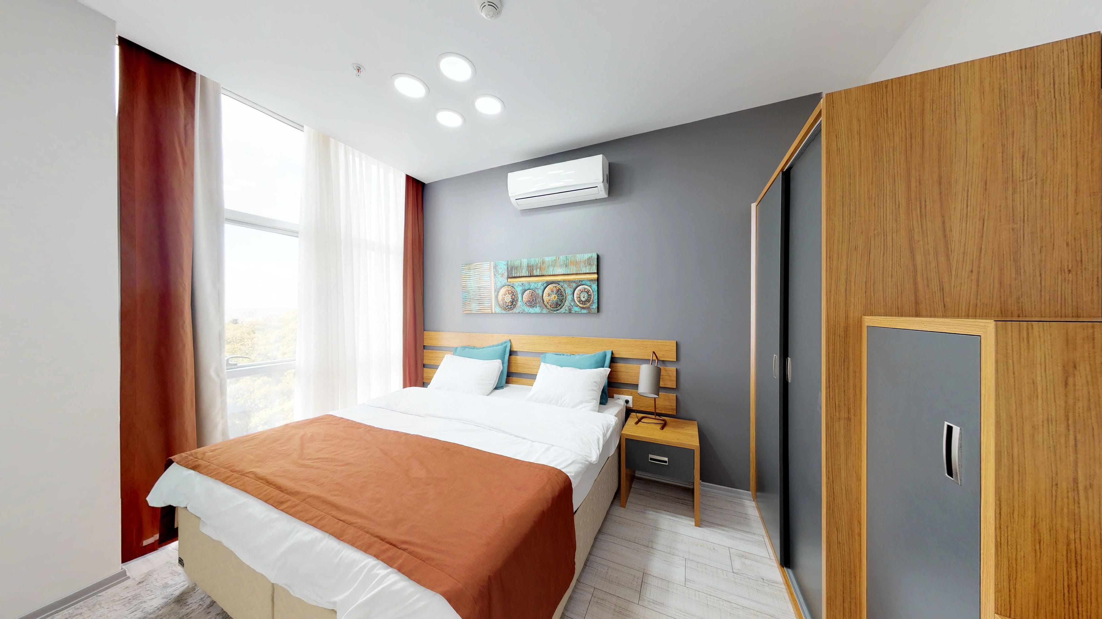 A modern bedroom with a bed, bedside tables, a wardrobe, and an air conditioning unit.