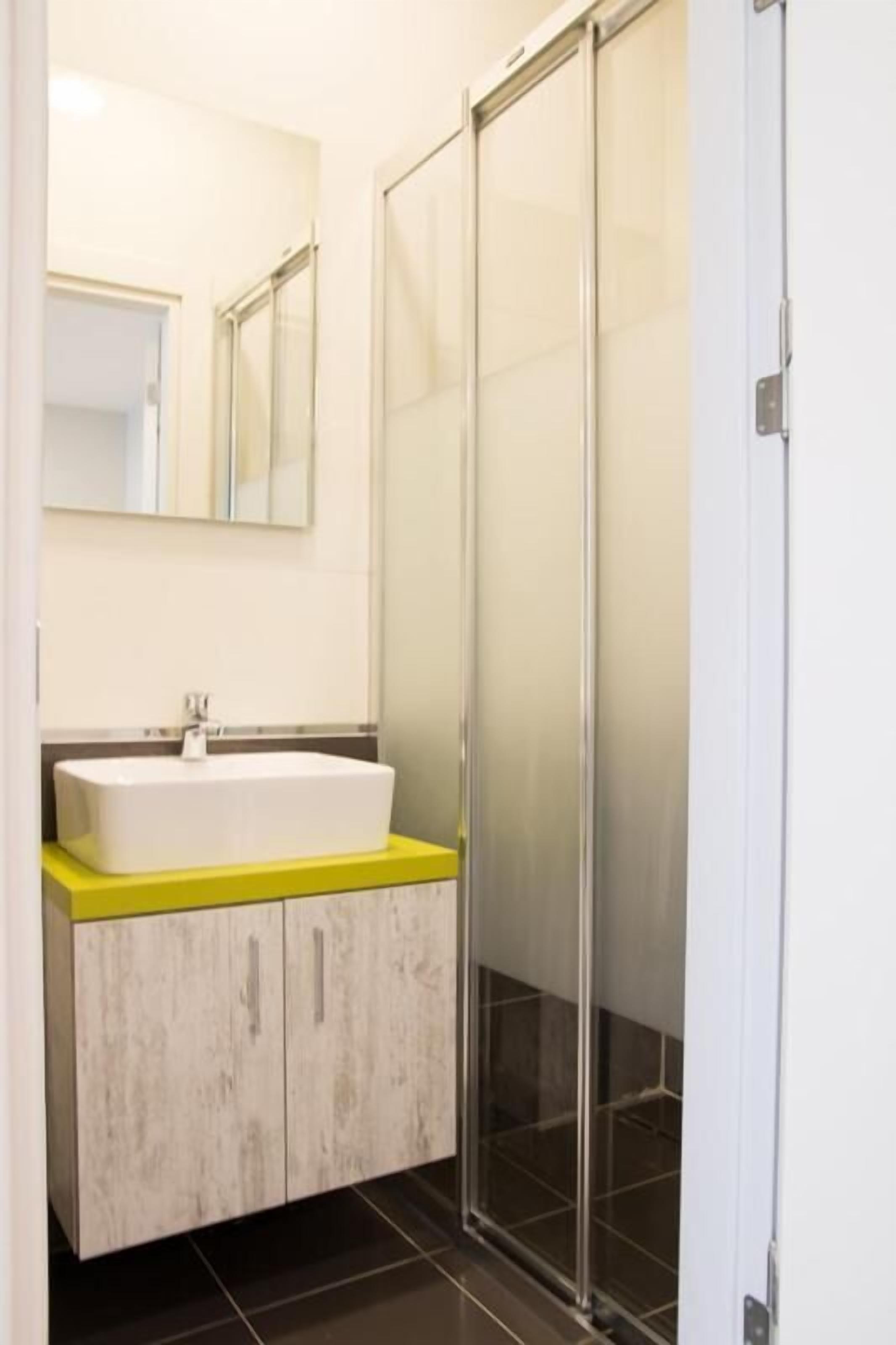 Un baño con lavamanos blanco, encimera amarilla y cabina de ducha de vidrio.