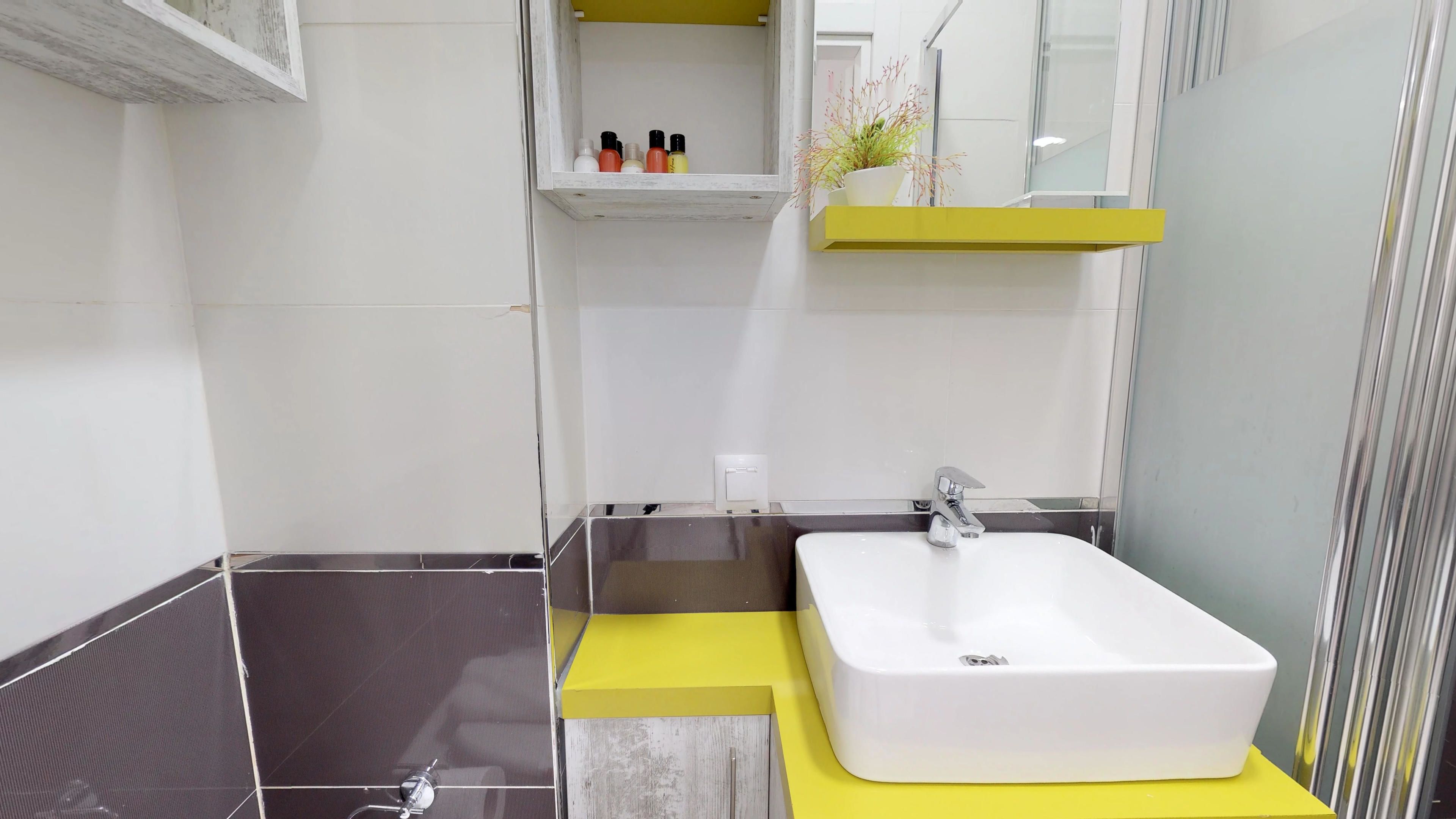 A modern bathroom with a white sink, yellow accents, and a mirror above the sink.