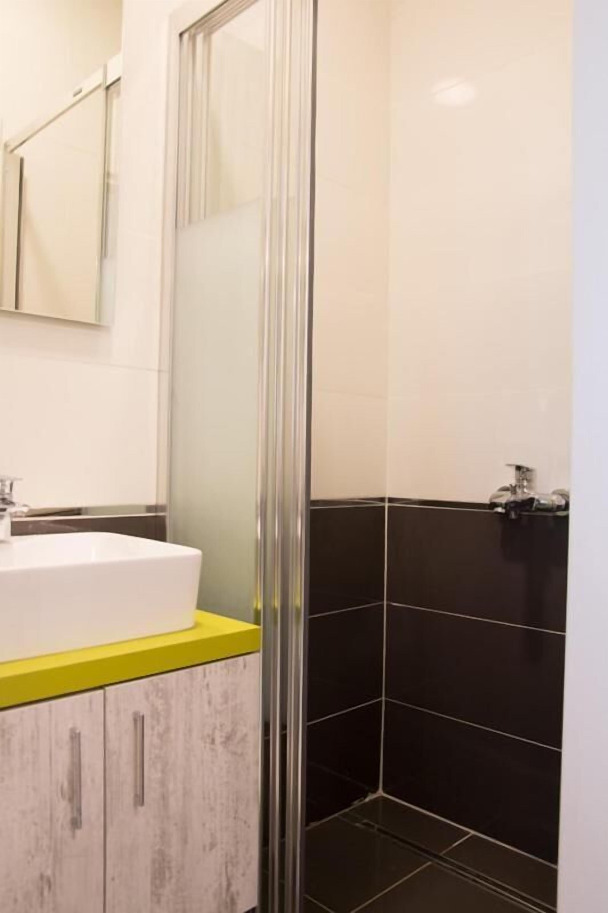 A modern bathroom with a white sink, yellow countertop, and black tiled walls.