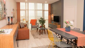 A modern living room with a sofa, dining table, and chairs, a TV, and a large window. - ZİN D Home Dudullu Suit Otel (Istanbul)