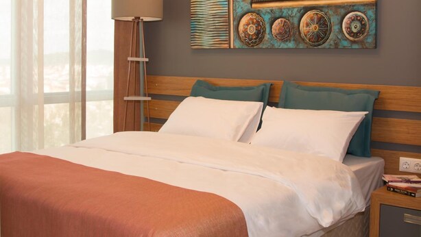 A hotel room with a bed, a nightstand, an air conditioner, and a window with curtains. - ZİN D Home Dudullu Suit Otel (Istanbul)